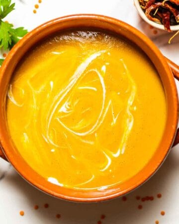 close-up of a bowl of lentil soup and heavy creamy on top with green herbs