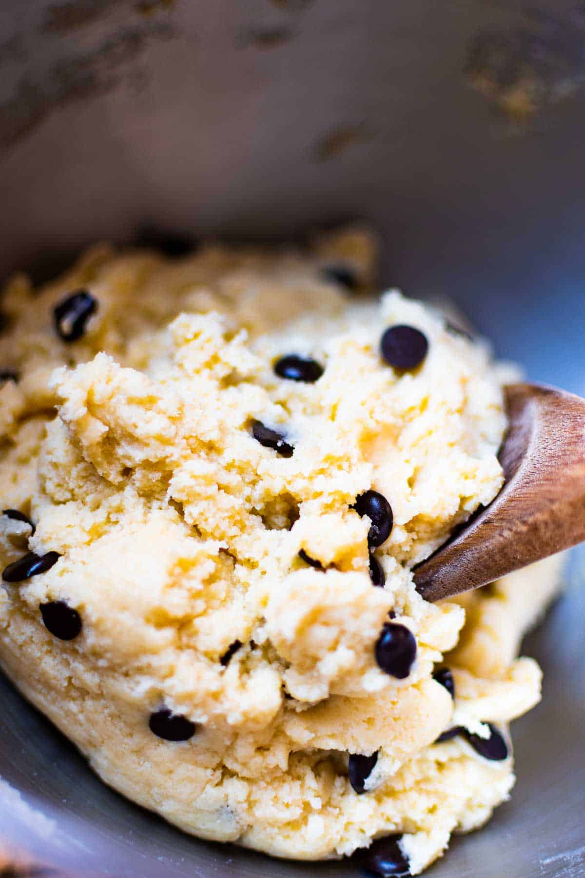 chocolate chip cookie dough in metallic bowl and a wooden spoon