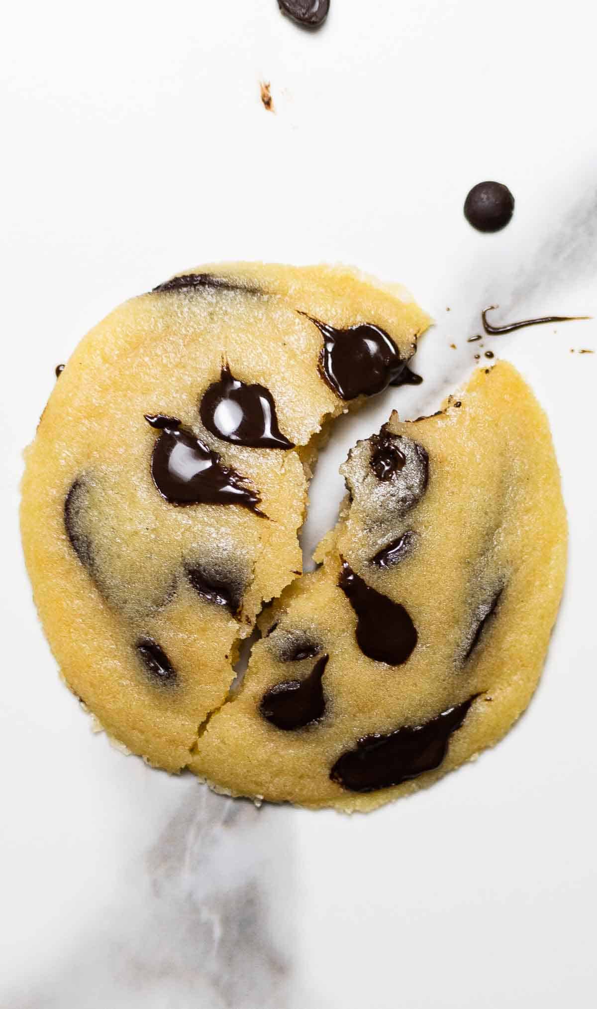 1 chocolate chip cookie broken in two halfs on white marble