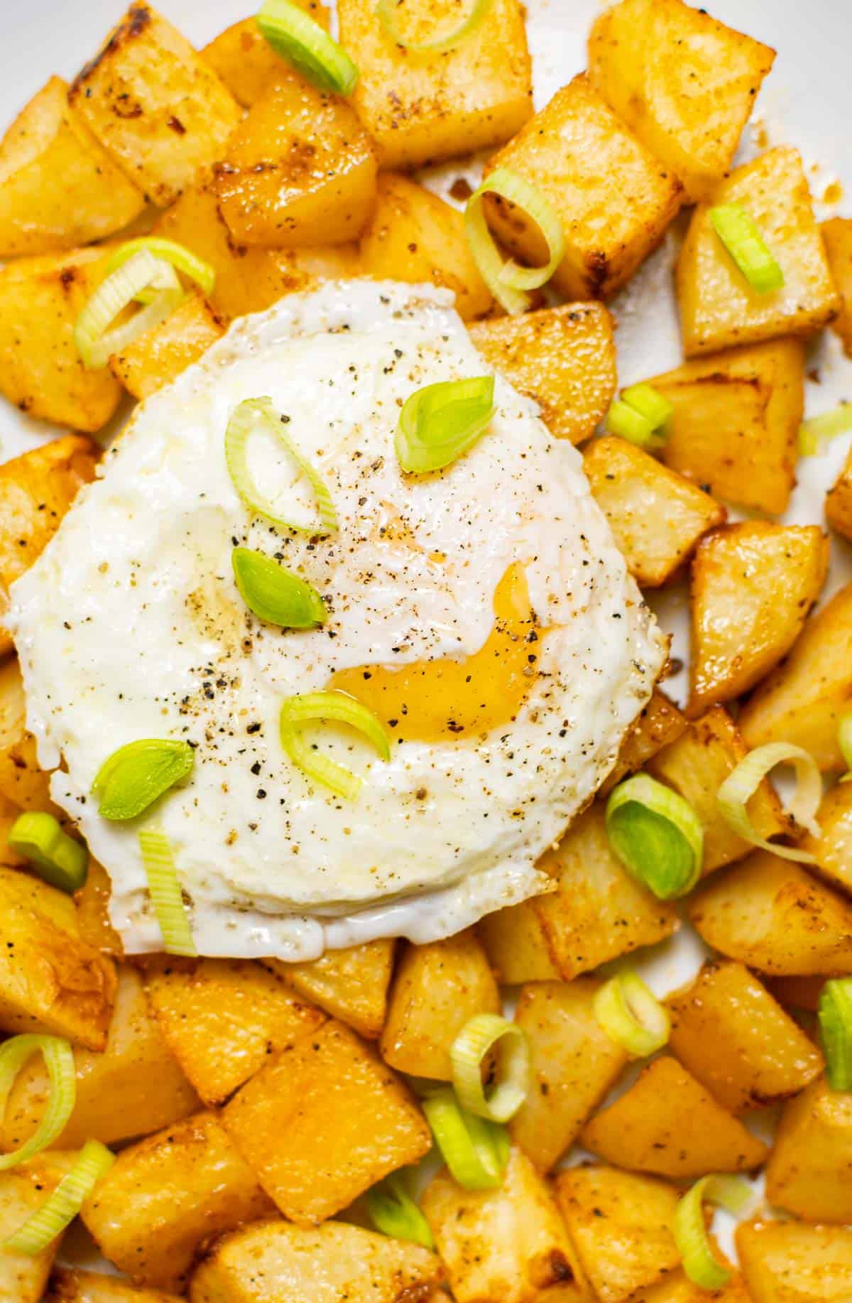 close-up of air fried breakfast potatoes with an egg on top and leeks.