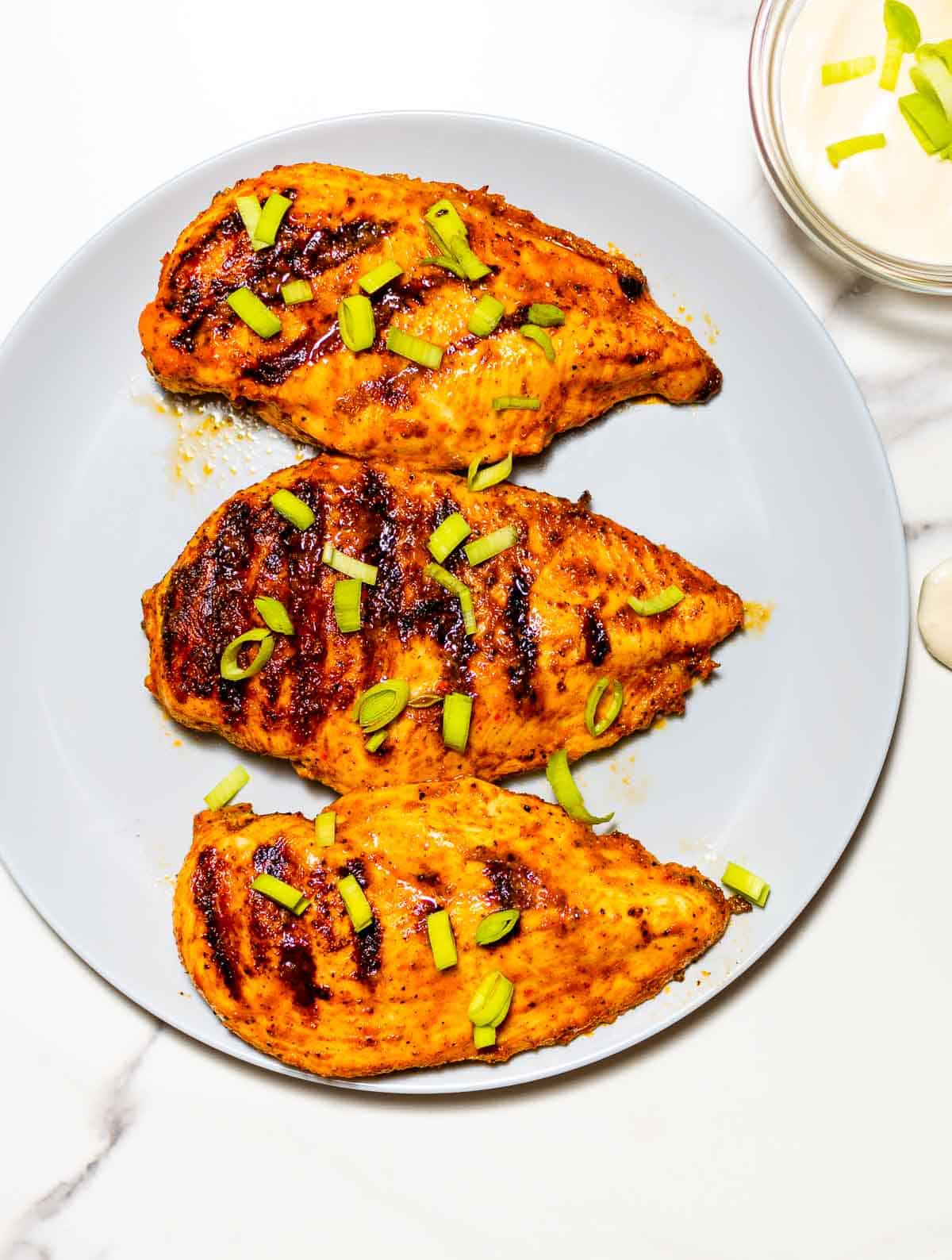 three grilled buffalo chicken breasts on a grey dish with green onion on top