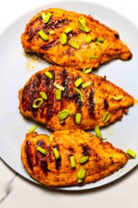 a close-up of three grilled chicken breasts on grey dish
