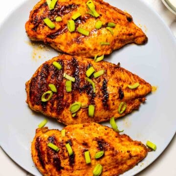 three grilled buffalo chicken breasts on a grey dish with green onion on top