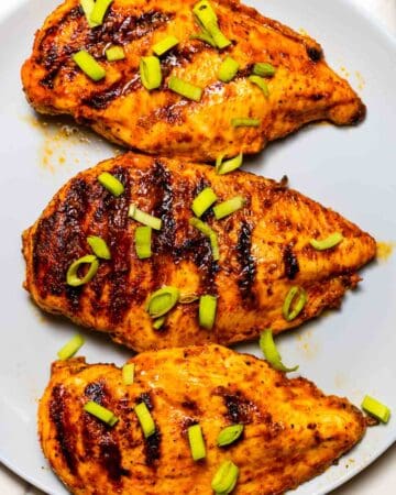 three grilled buffalo chicken breasts on a grey dish with green onion on top