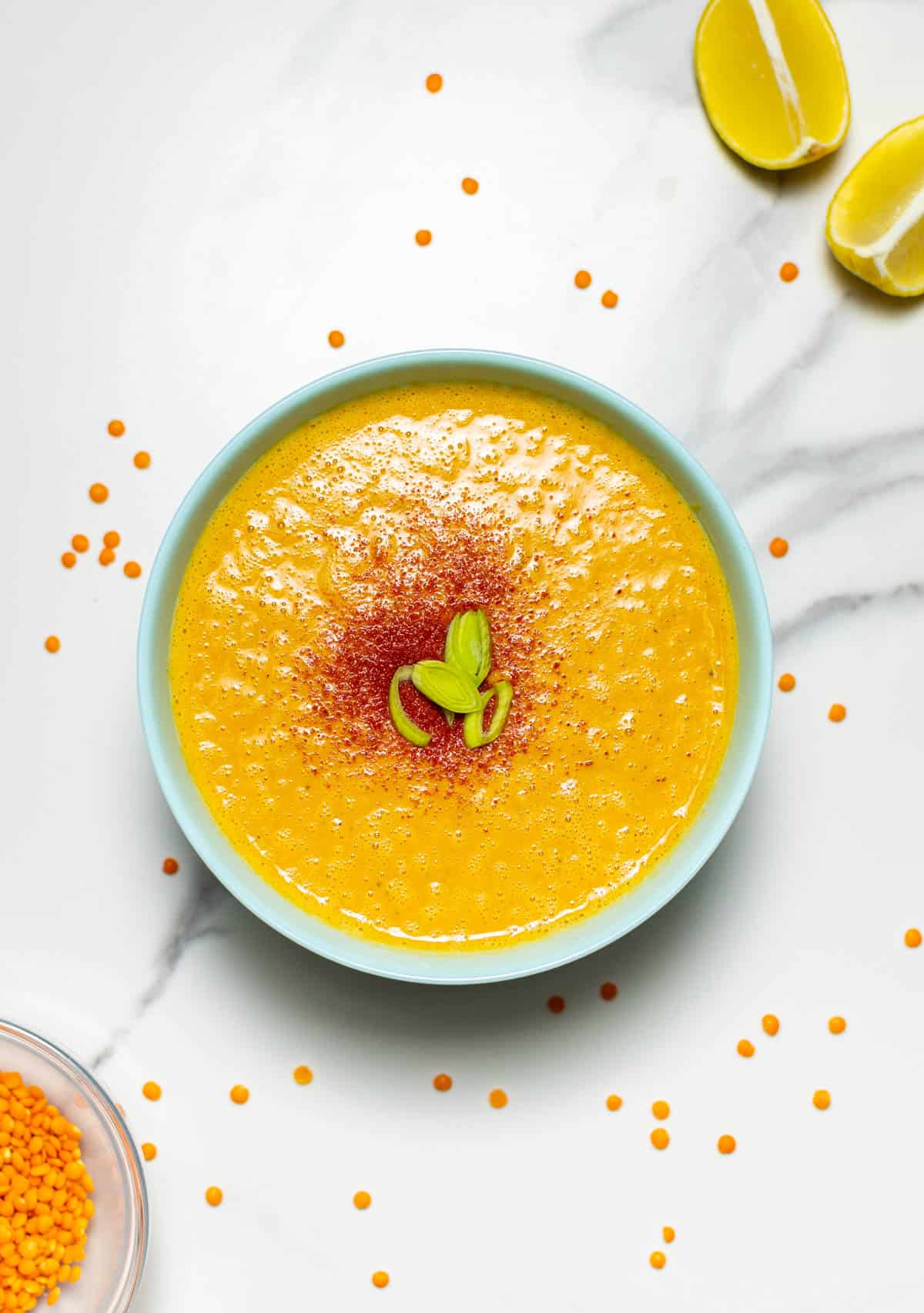 overlay shot of a bowl of red lentil soup with a slice of lemon on the side