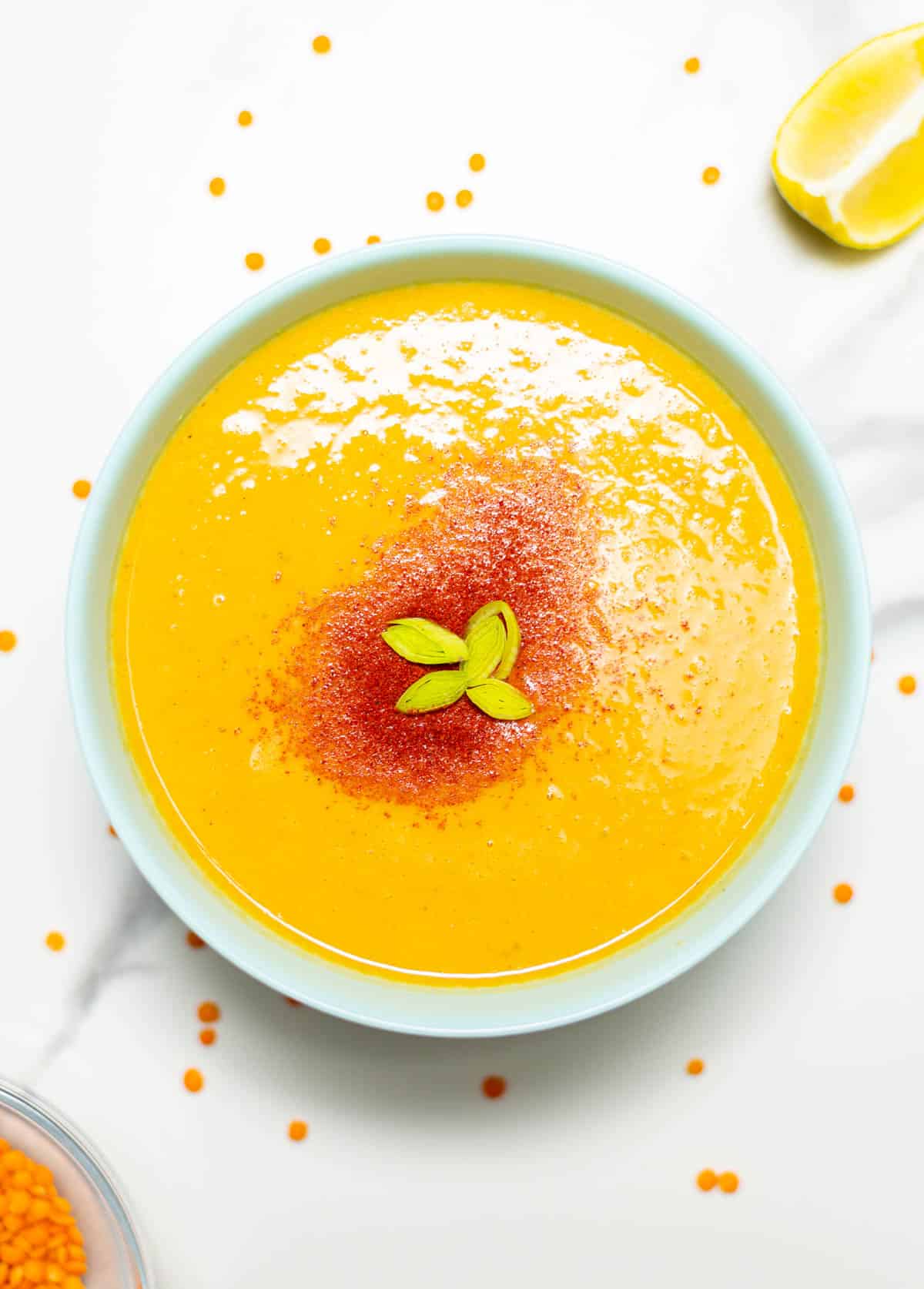 overlay shot of a bowl of red lentil soup with a slice of lemon on the side