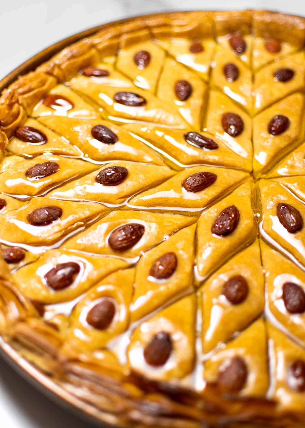 a close-up of a baking dish full of authentic baklava with almonds on top
