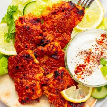 Greek yogurt marinated chicken on a platter with garnish.