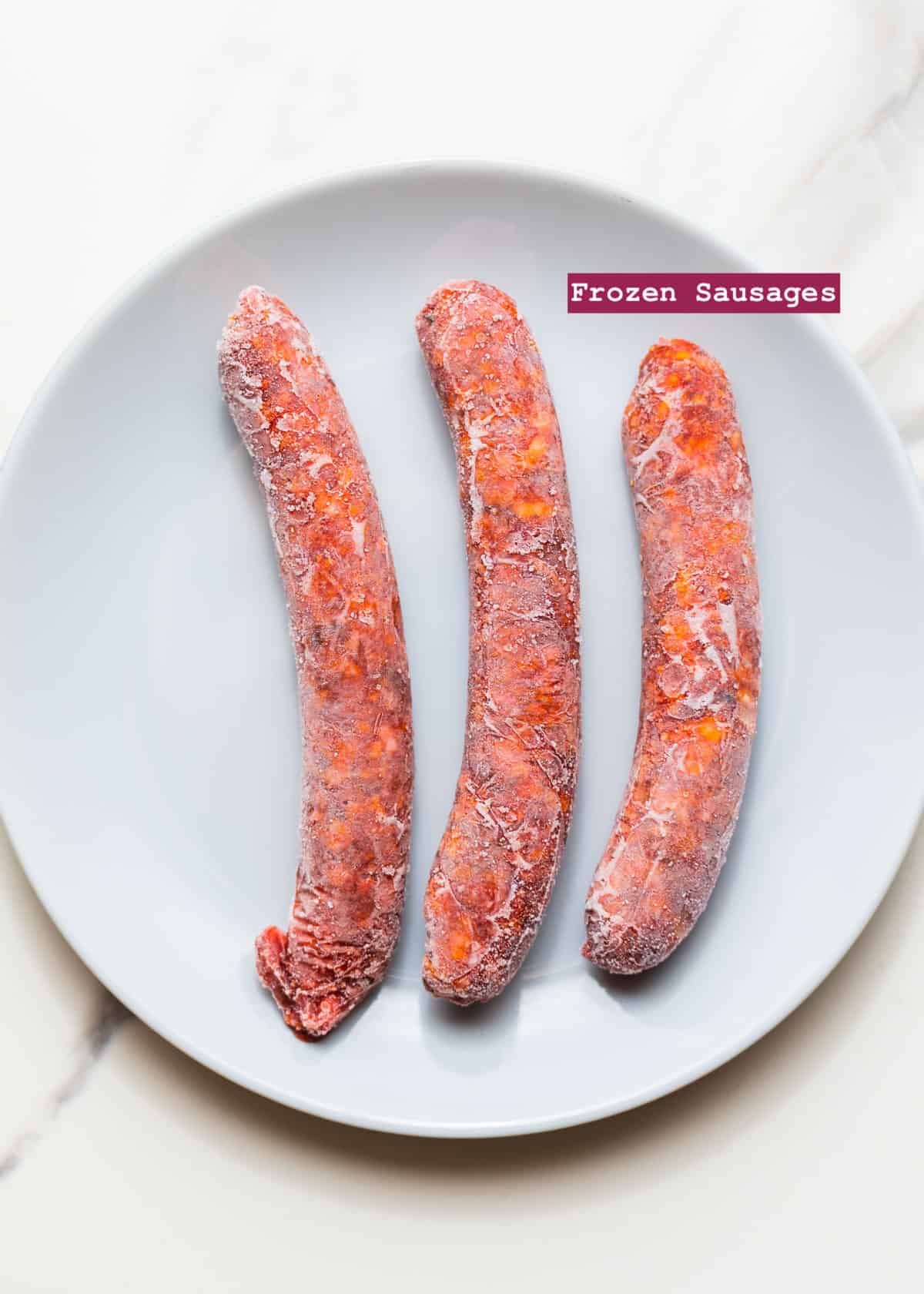 three frozen sausages in a grey dish on a white surface.