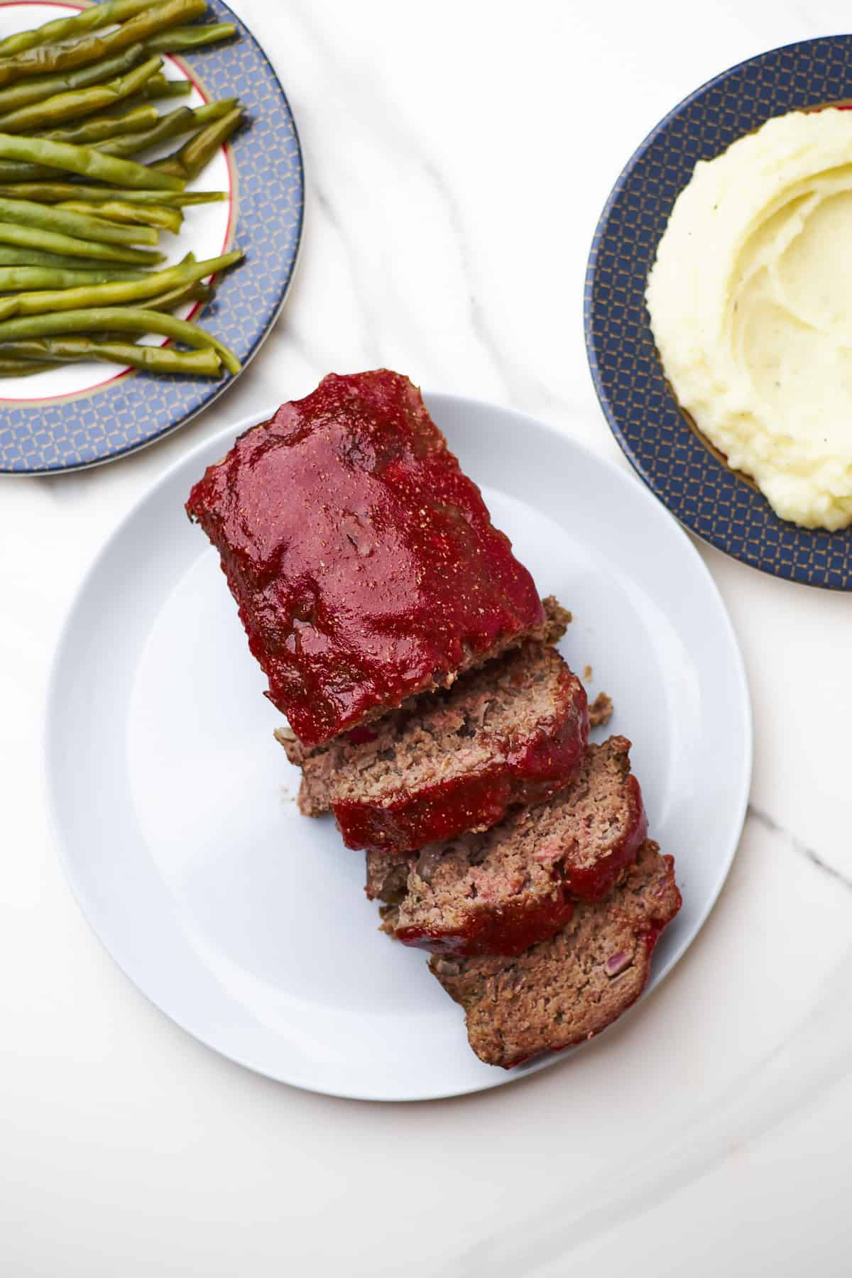 sliced lipton onion soup meatloaf on serving platter with mashed potatoes and green beans on the side.