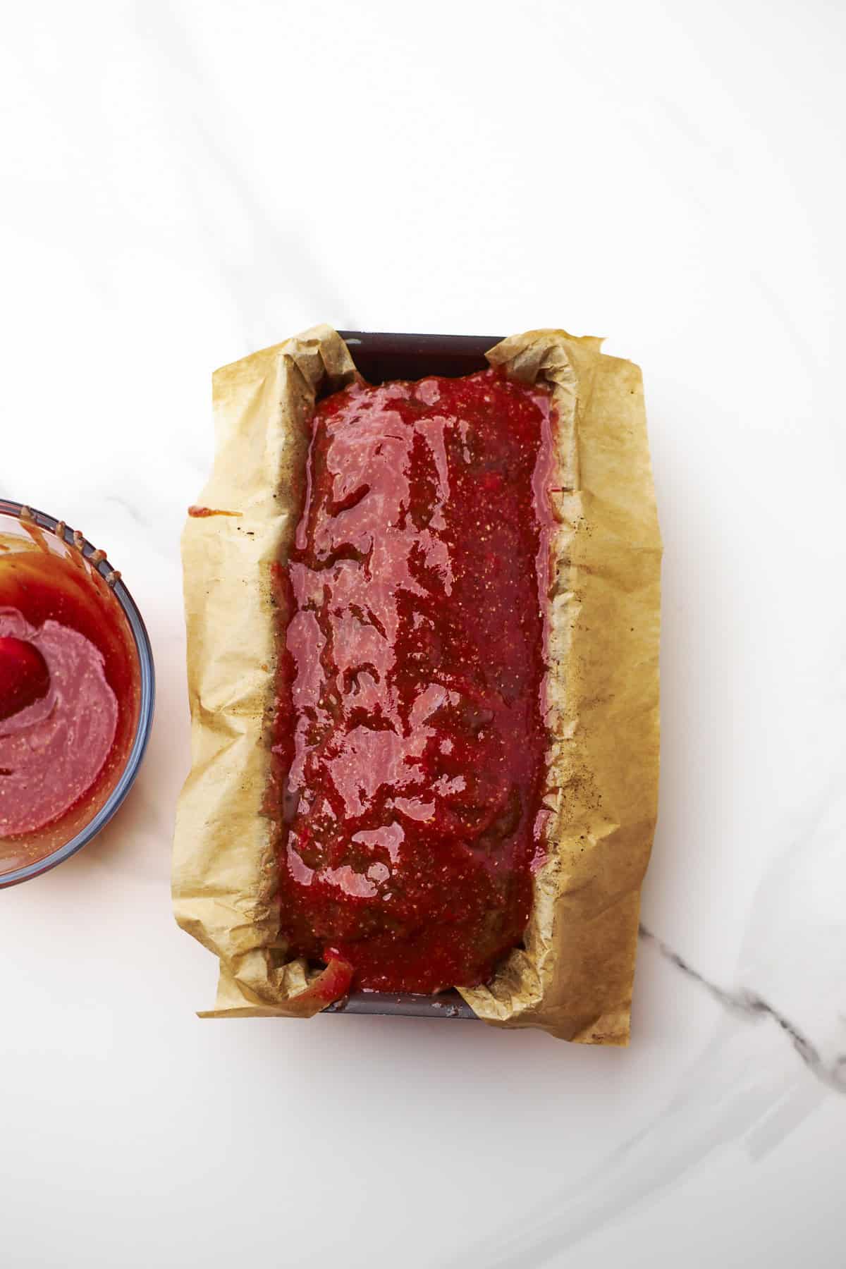 glazed meatloaf in a baking pan ready for baking.