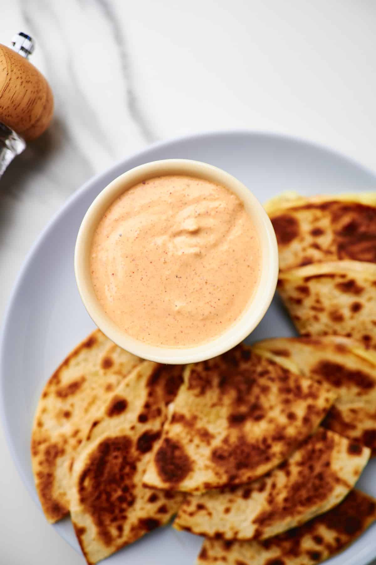 Small bowl filled with quesadilla sauce on a plate with quesadillas.