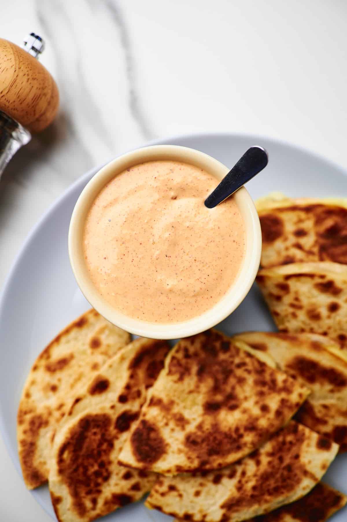 Small bowl filled with quesadilla sauce on a plate with quesadillas.