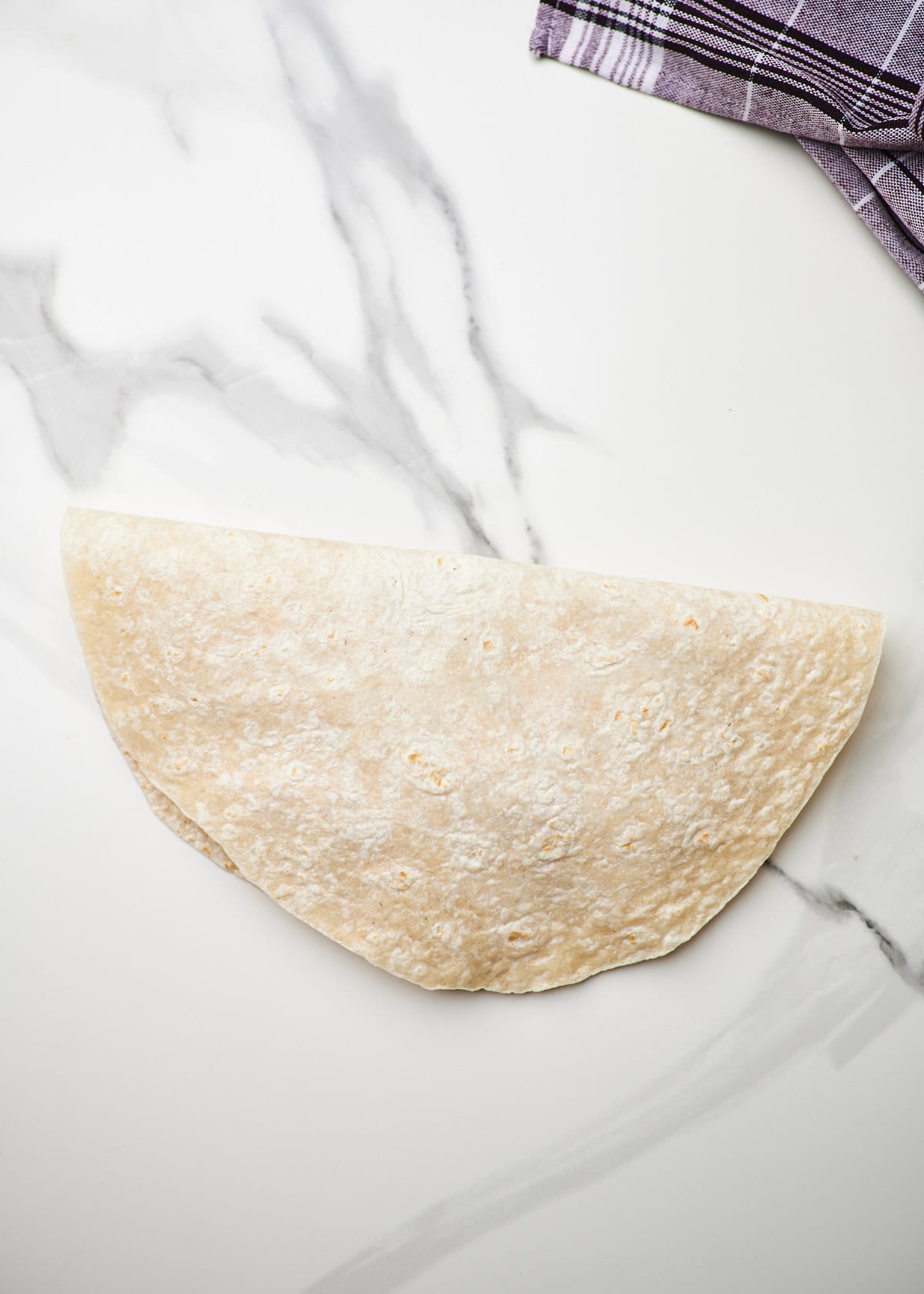 A cheesy chicken quesadilla folded over and ready to go in the pan to cook.