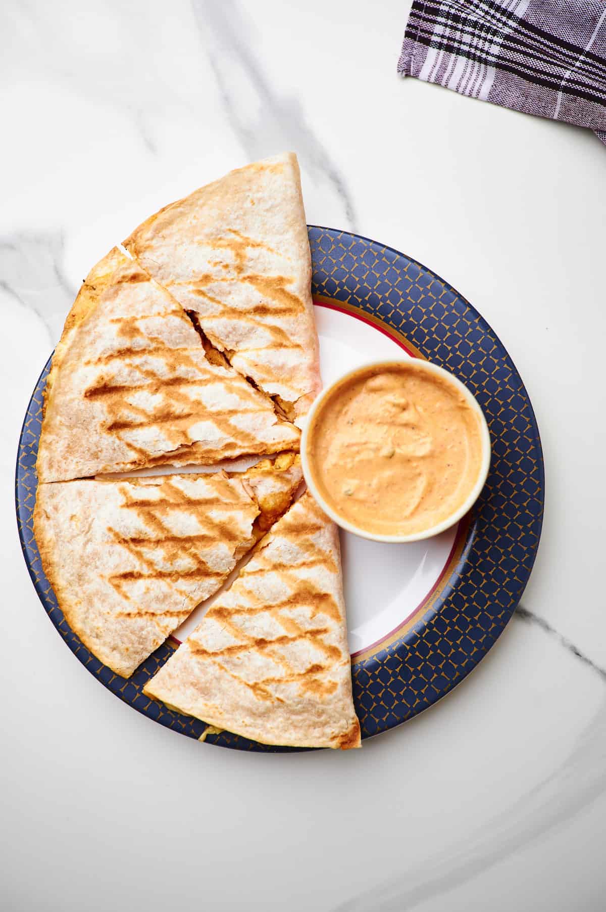 Copycat Taco Bell chicken quesadilla on a plate with a small bowl of quesasdilla sauce.