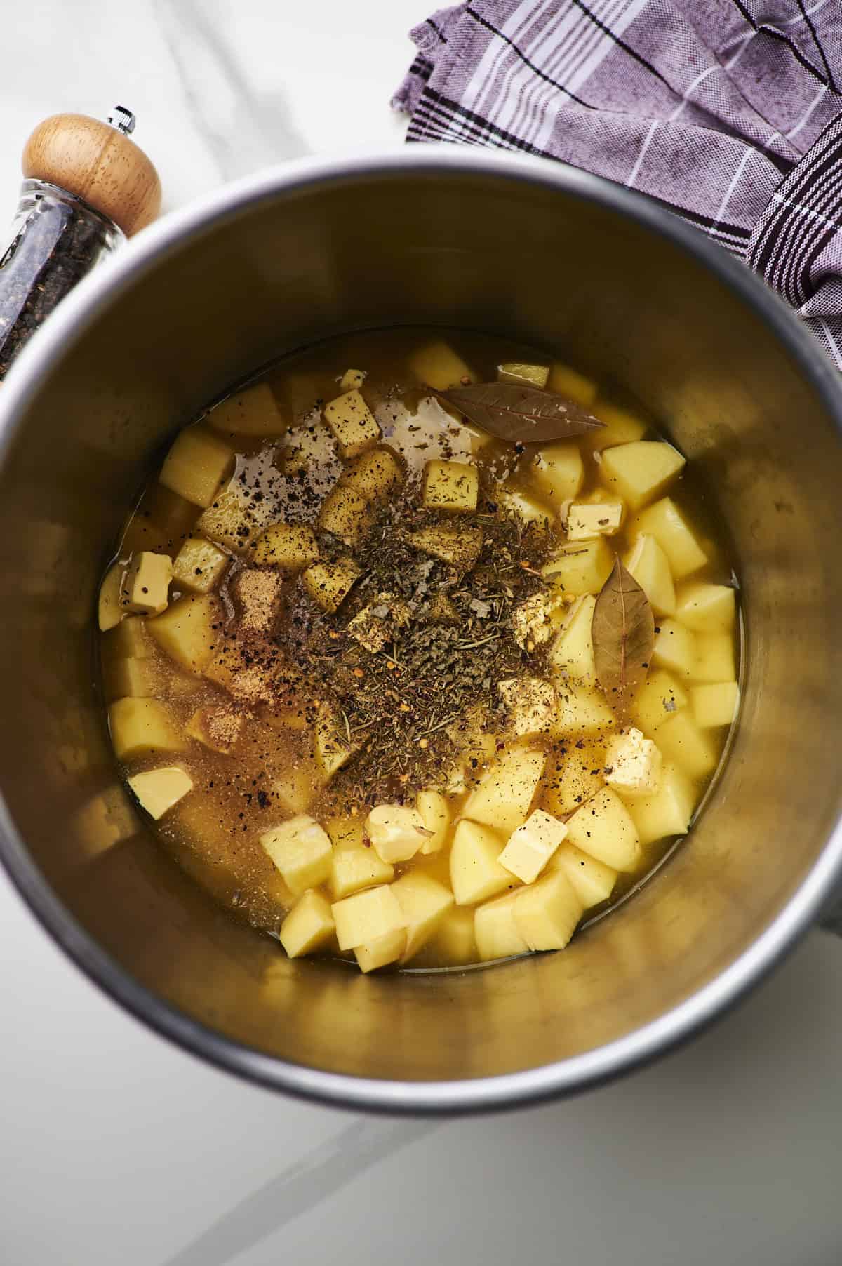 Instant pot insert filled with diced potatoes, diced butter, and dried herbs.