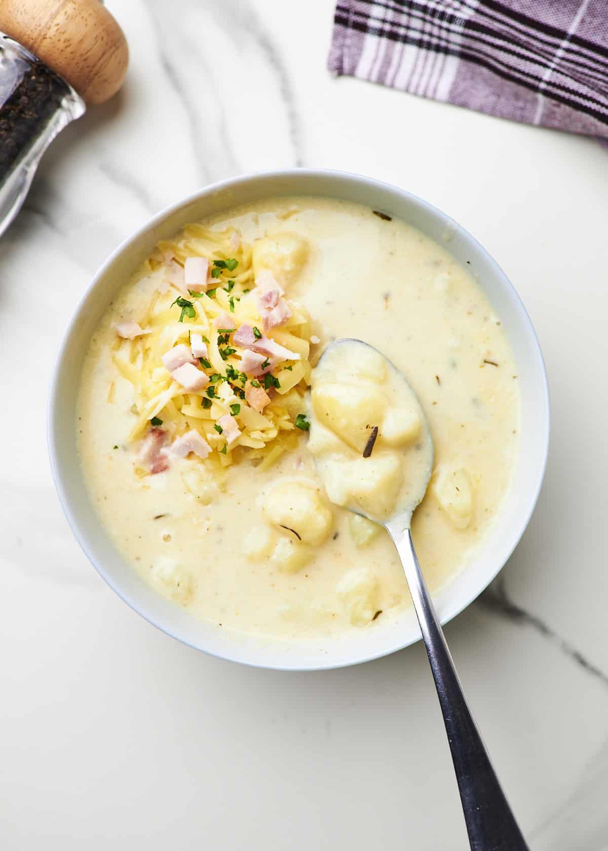 Small bowl filled with creamy potato soup garnished with shredded cheese, and crumbled smoked chicken.