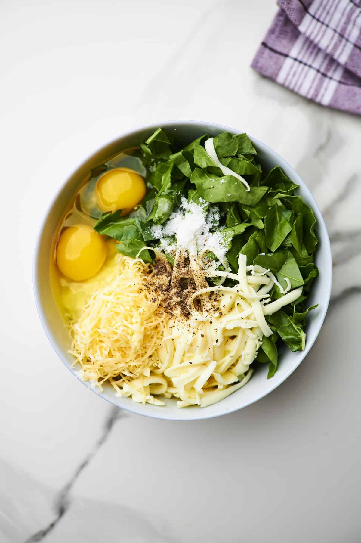 Large white bowl filled with cheesy lasagna filling ingredients