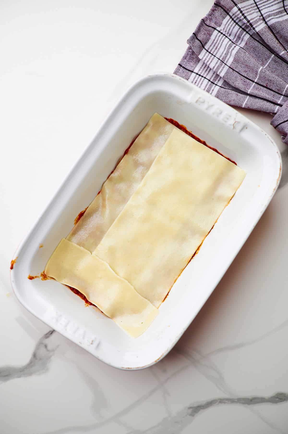 White baking dish with meat sauce and cooked lasagna noodles