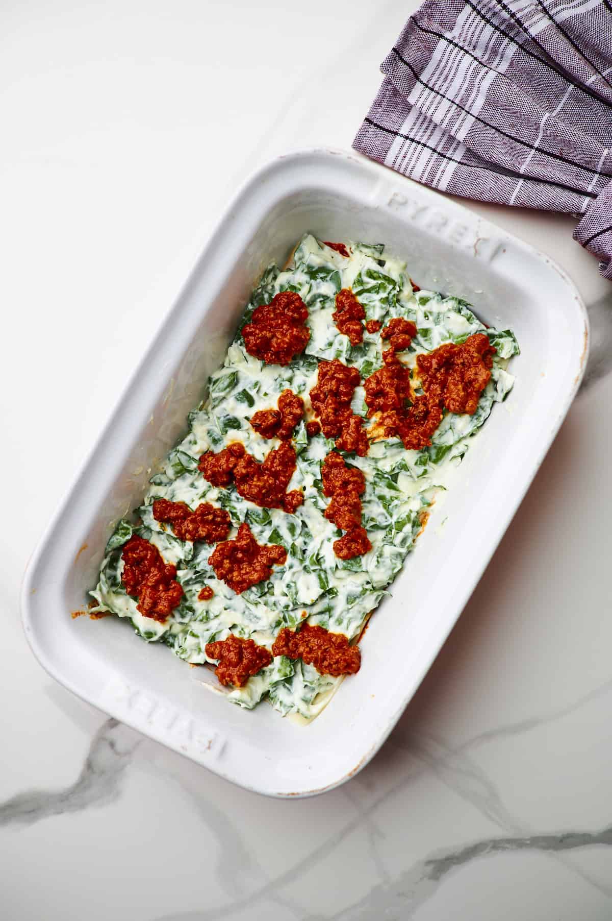 White baking dish filled with ingredients to make meaty cottage cheese lasagna