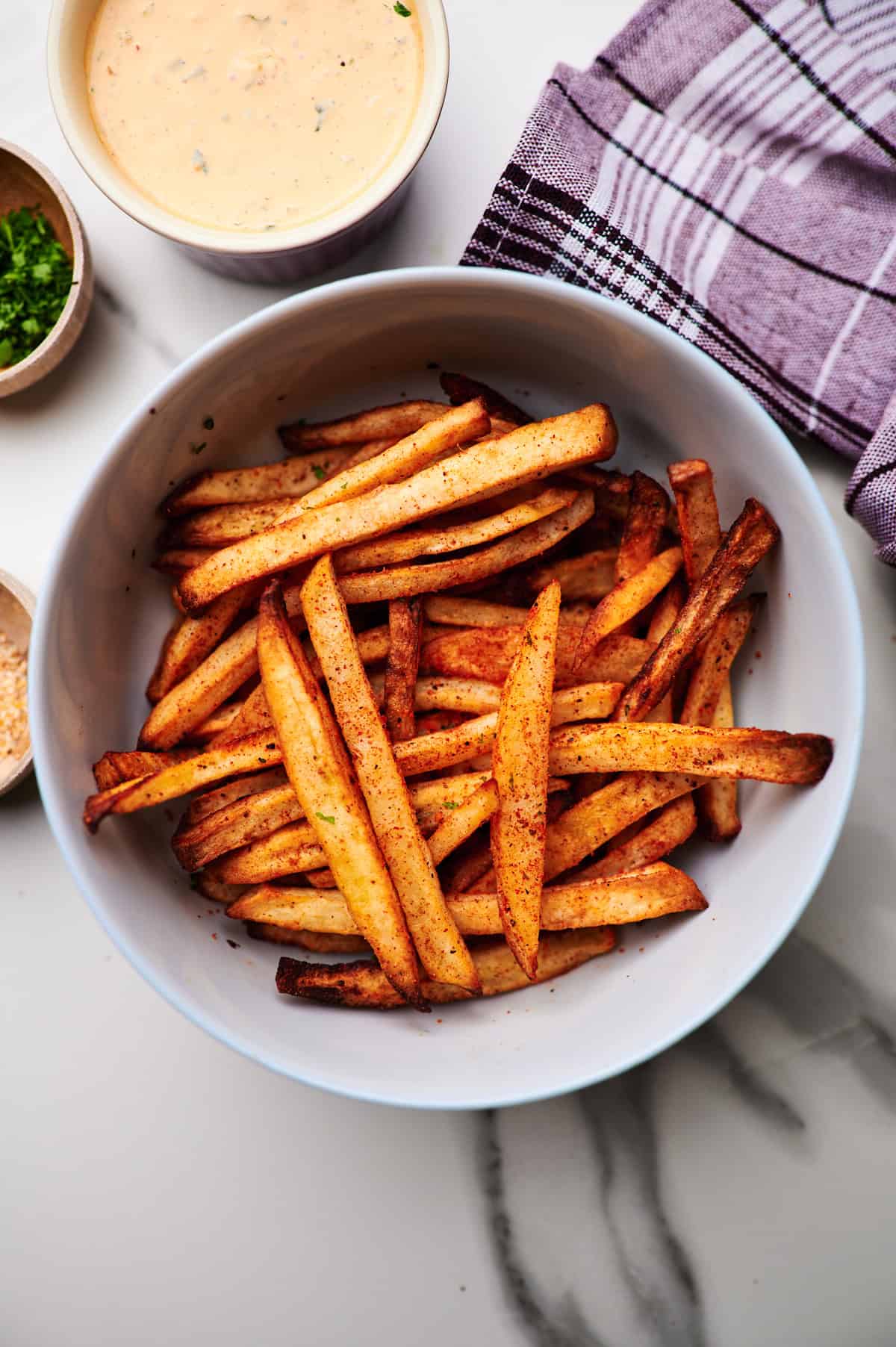 frozen french fries from air fryer with garlic salt, parmesan cheese and italian parsley in bowl on countertop.