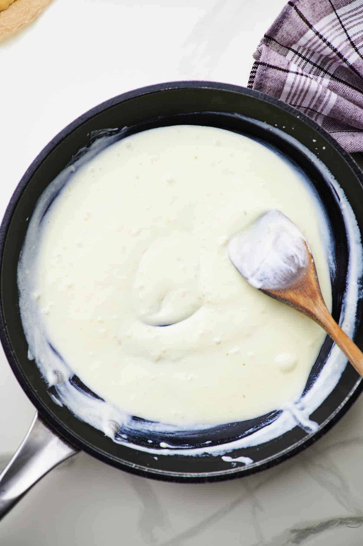 greek yogurt being stirred into healthier alfredo sauce in a pan