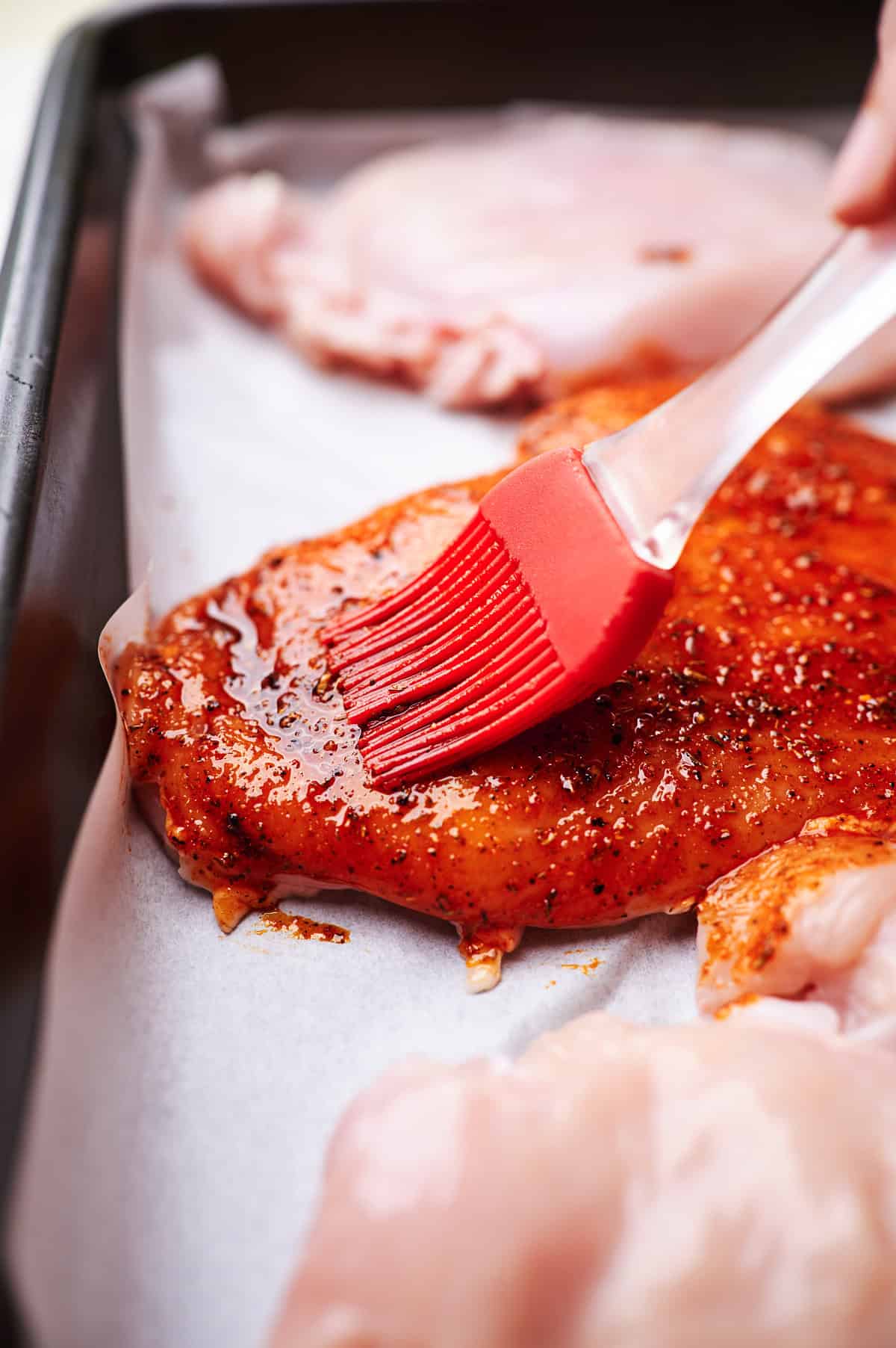 Seasoning chicken breasts with a red brush in a baking dish.	