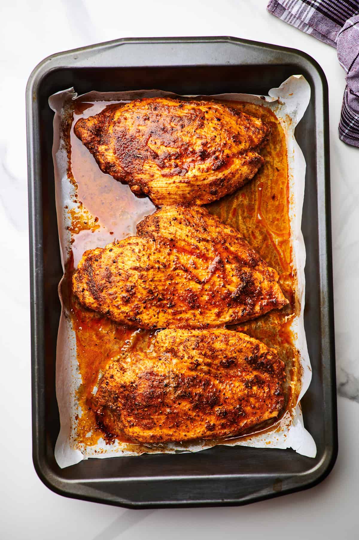 Overhead view of baked chicken breasts in a white baking dish.