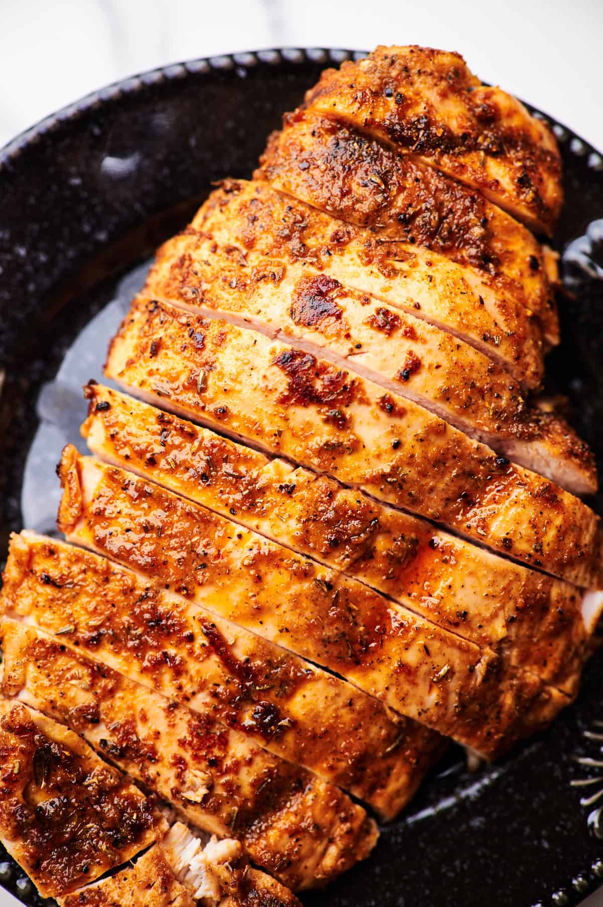 Overhead view of sliced baked chicken breasts on a serving plate. 