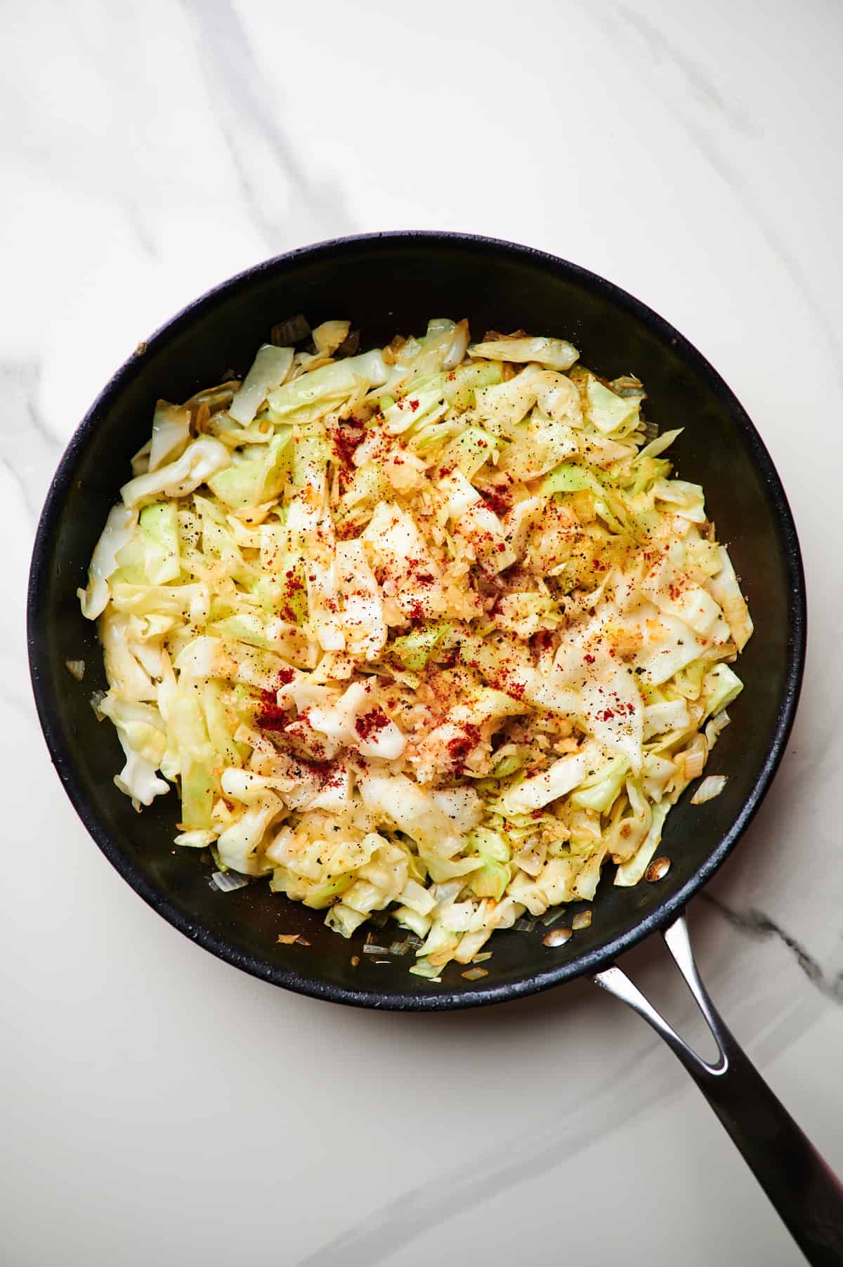 adding paprika and chicken to a skillet with sauteed cabbage