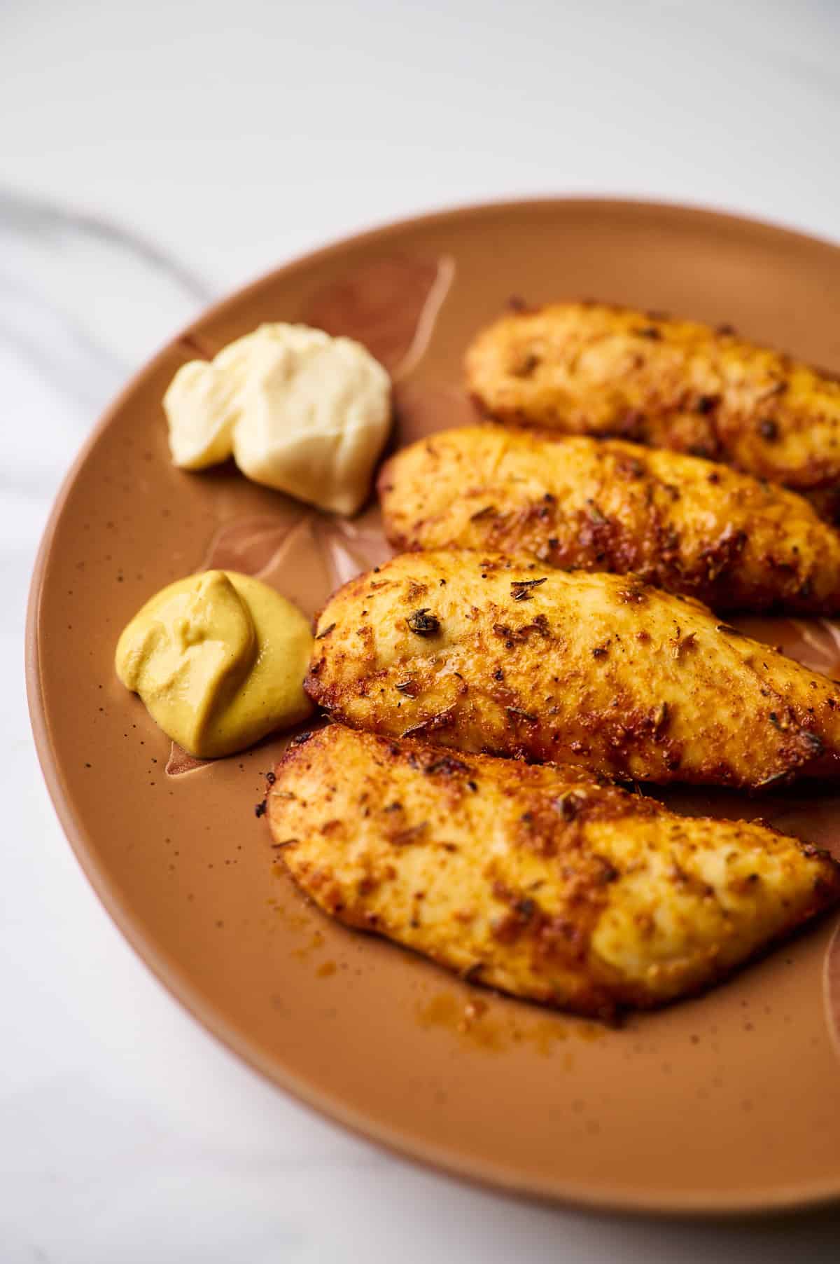 side view shot of an Air fryer chicken tenderloins served with mayo and dijon mustard on a brown plate